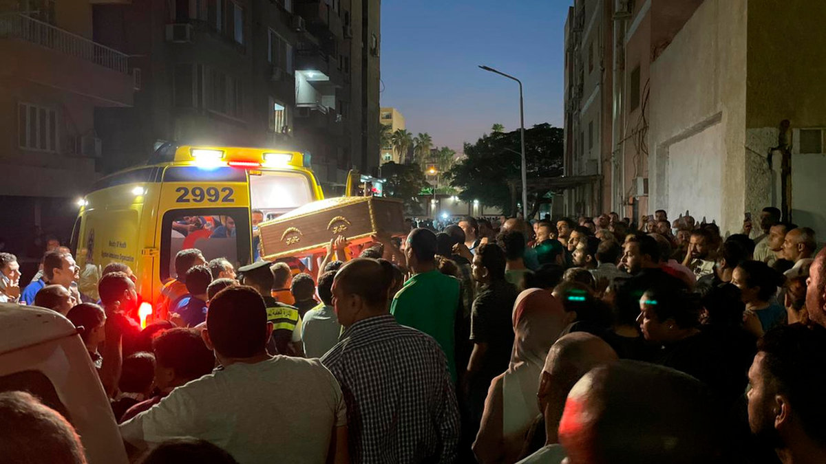 En kista bärs in i en ambulans medan folk samlas för en minnesgudstjänst för offren i branden, sent på söndagskvällen.