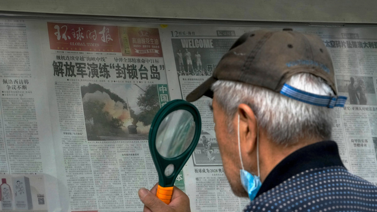 En man använder förstoringsglas för att läsa om Kinas militärövning runt Taiwan under söndagen.