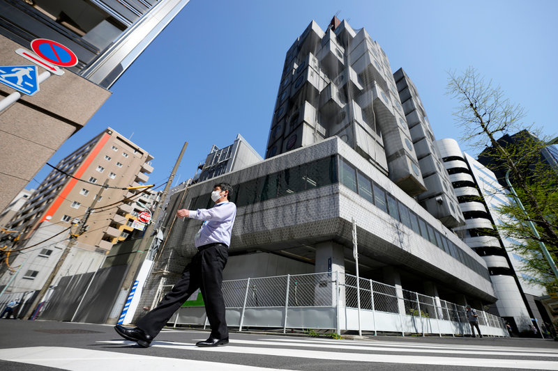 En man går förbi Nakagin-tornet i Tokyo, som nu försetts med nät och börjats monteras ner.