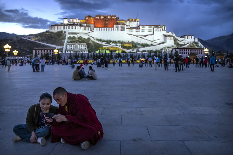 En munk och en kvinna tittar på en mobiltelefon framför Potalapalatset i Lhasa i Tibet, som ses som tibetanernas högste andlige ledare Dalai lamas traditionella hem. Bilden togs 2021. 