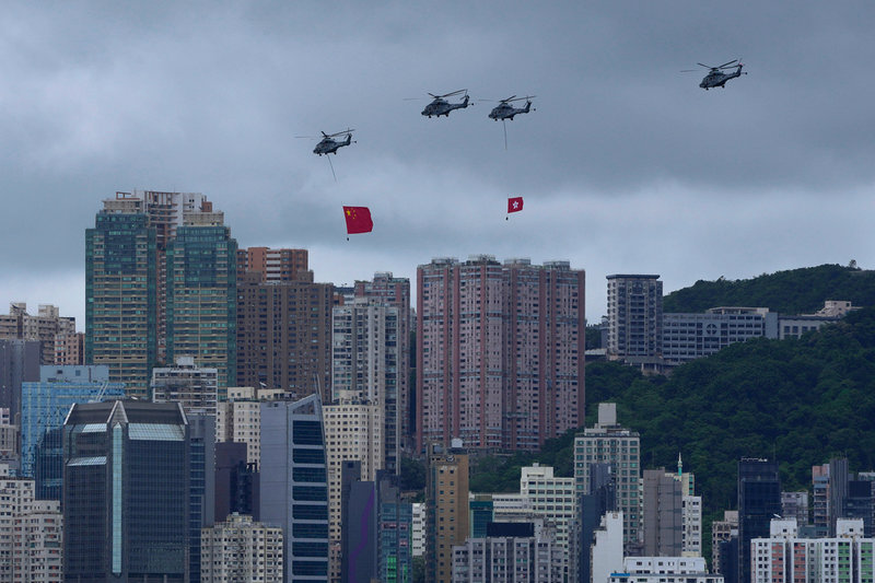 Helikoptrar flyger fram över Hongkong med två flaggor: en stor kinesisk och en mindre Hongkong-flagga.
