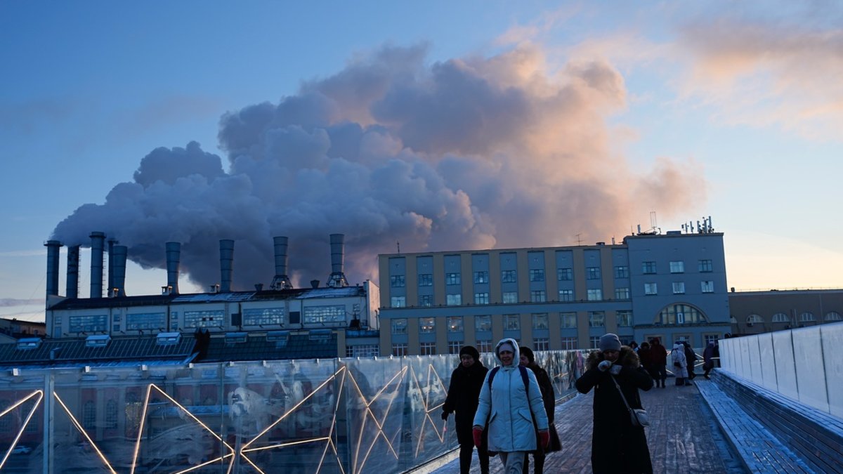 En grupp människor går över bron vid Zarjadjeparken i Moskva med ett av stadens värmeverk i bakgrunden. Många av de ryska värmeverken har den senaste tiden drabbats av haverier.