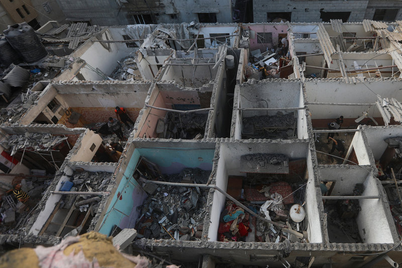 Palestinier går igenom rasmassor som återstår av ett stort bostadshus i som bombats sönder i Rafah. Bilden togs under tisdagen.