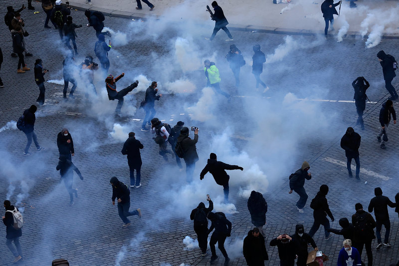Svartklädda ungdomar försöker sparka bort tårgasbehållare efter en sammandrabbning med polis i Paris.