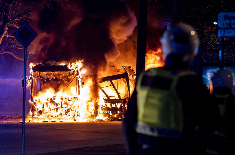 Kravallpolis framför en brinnande stadsbuss i Rosengård i Malmö, i samband med påskupploppen. Arkivbild.