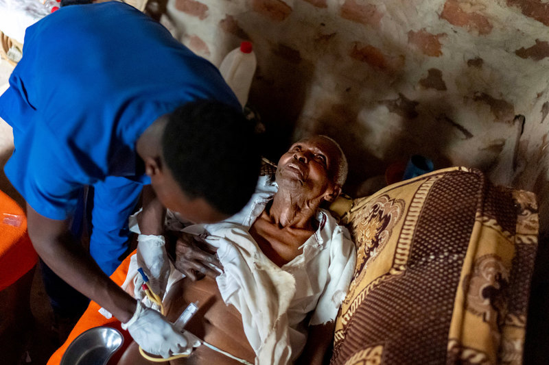 Fältsjukskötaren Derrick Ssemanda vid hjälporganisationen Rotom byter kateter på 86-årige Yafesi Nakyanga under ett hembesök i Nabalanga, Uganda.