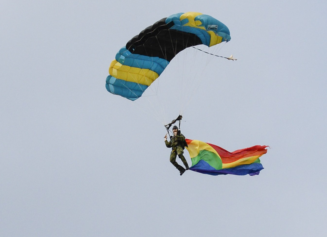 En person hoppar fallskärm och viftar Prideflaggan. En person hoppar fallskärm och viftar Prideflaggan.