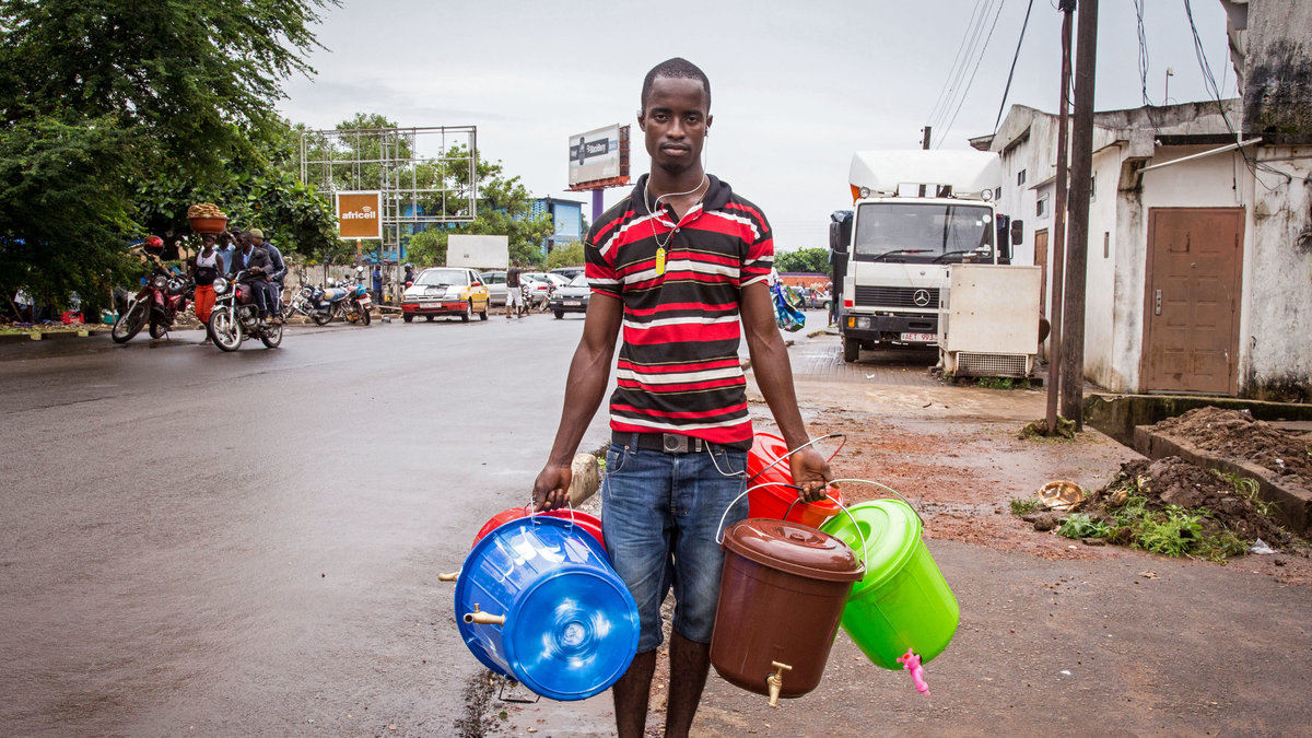 En gatuförsäljare i Sierra Leone säljer vattenhinkar till för att tvätta händerna.