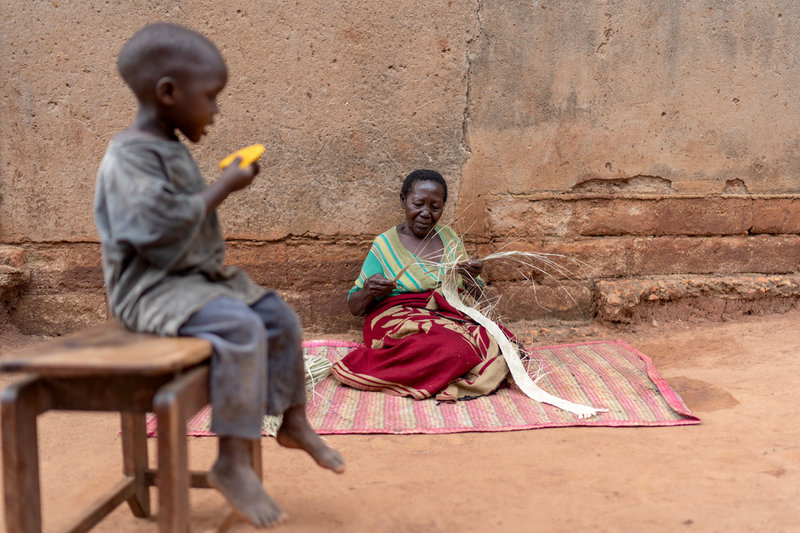 75-åriga Tereza Nabunya flätar mattor från papyrus utanför sitt hus i Nkulagirire, Uganda för att sälja och kunna betala för ett läkarbesök.