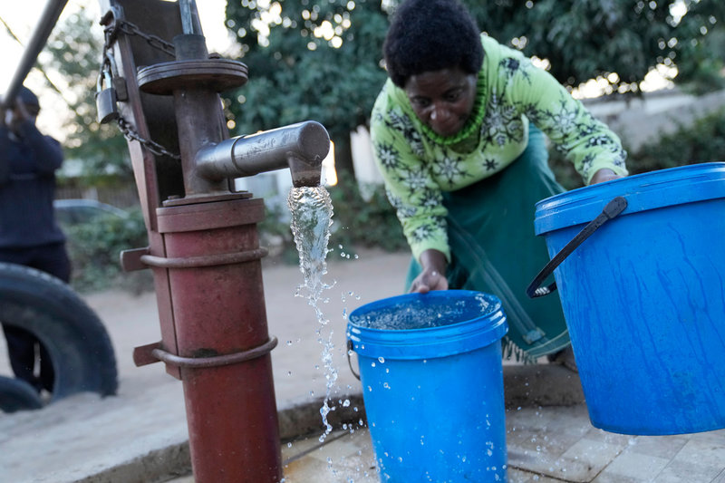 Jeffrey (skymd till vänster) och Christwish Carlos hämtar vatten i sitt bostadsområde i Harares utkanter.