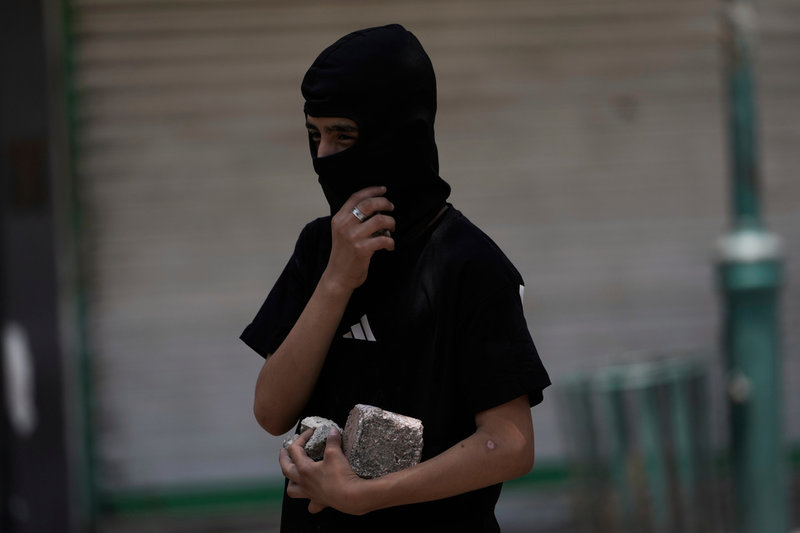 En maskerad palestinier bär på stenar under en konfrontation med israeliska soldater i Nablus på tisdagen.