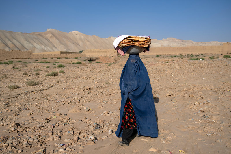 En kvinna med nyinhandlat bröd nära Bamiyan i juni 2023. Hon bär burka, ett heltäckande plagg som talibanerna kräver att kvinnor har på sig när de lämnar hemmet.