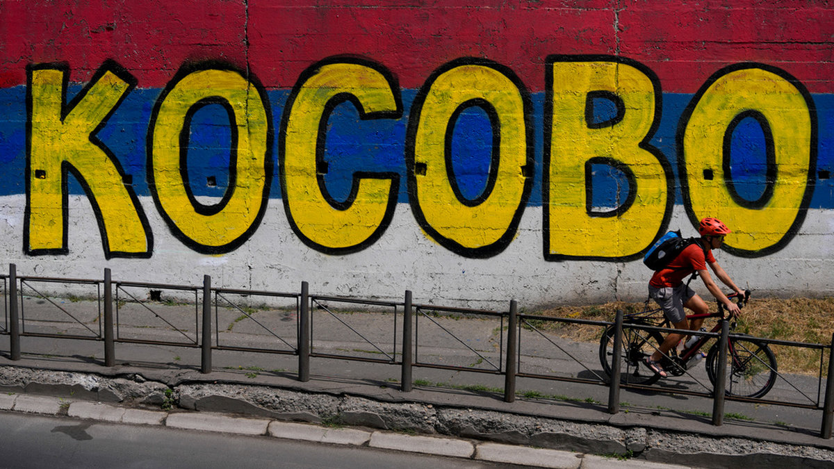 En man cyklar förbi en väggmålning i Serbiens huvudstad Belgrad med texten 'Kosovo' målat ovanpå den serbiska flaggans färger. Arkivbild.
