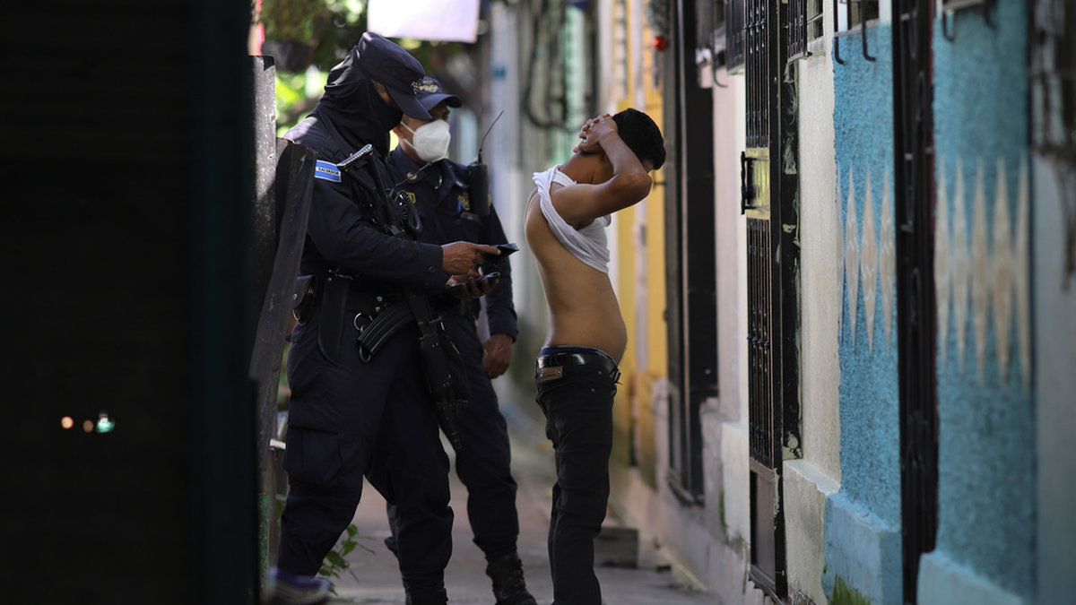 Poliser kroppsvisiterar en man under en sökinsats efter gängmedlemmar i Soyapango utanför San Salvador den 16 augusti.