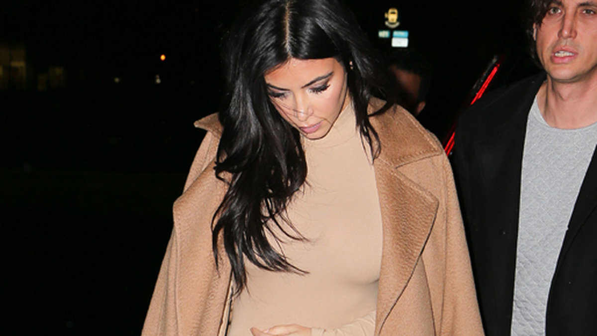 Kim Kardashian i beige kappa, ljus klänning och sexiga klackar. 