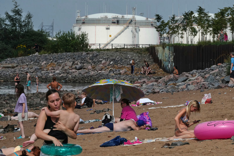 Människor solar och badar i närheten av oljeanläggningen i S:t Petersburg hamn i fjol. Anläggningen angreps av Ukraina tidigare i juni.