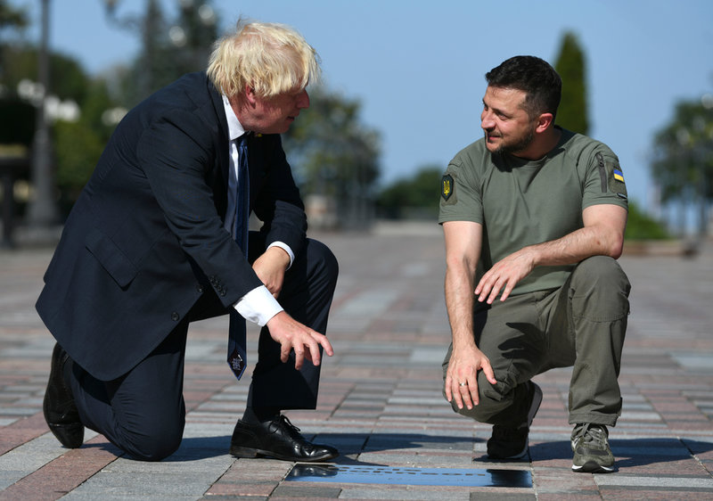 Storbritanniens premiärminister Boris Johnson och Ukrainas president Volodymyr Zelenskyj på plats i Kiev. De tittar på en skylt där personer som hjälpt till i kampen mot den ryska invasionen av Ukraina uppmärksammas.