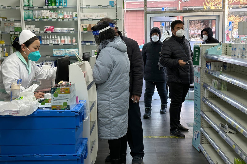 Människor med munskydd köar för att köpa läkemedel i ett apotek i Peking där hyllorna börjar eka tomma.