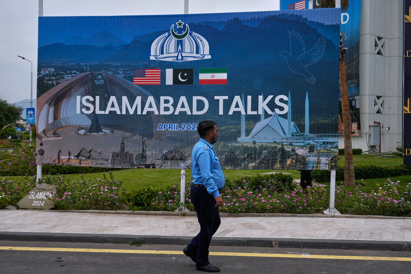 En polis i Islamabad passerar en skylt om  fredssamtalen mellan USA och Iran.