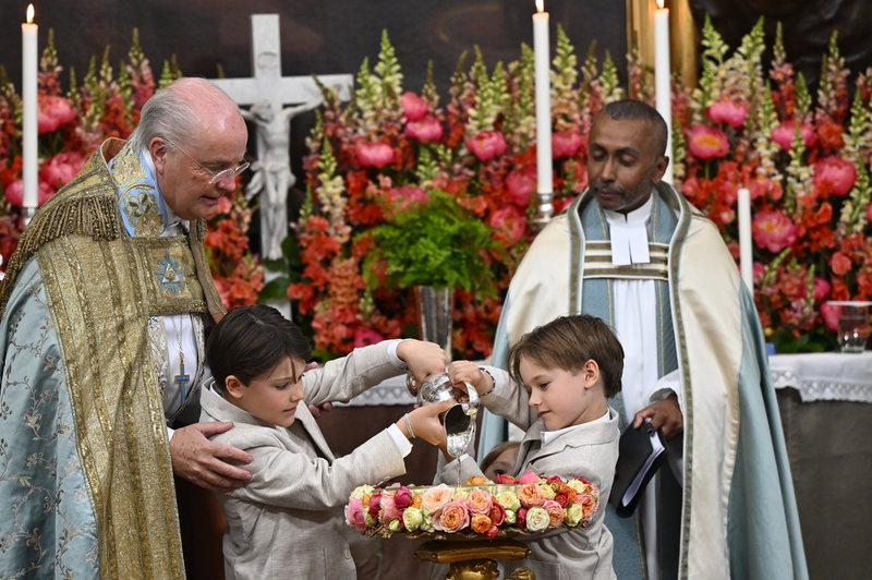 Dopförrättarna, överhovpredikant Johan Dalman och pastorn i Kungliga Hovförsamlingen Michael Bjerkhagen, överser när prinsarna Alexander och Gabriel häller upp dopvattnet.