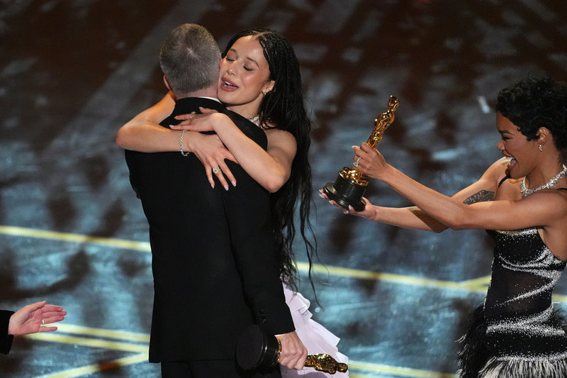 Chase Infiniti kramar om regissören Paul Thomas Anderson när "One battle after another" får priset för bästa film på Oscarsgalan. Bredvid står skådespelaren Teyana Taylor med Oscarsstatyetten.