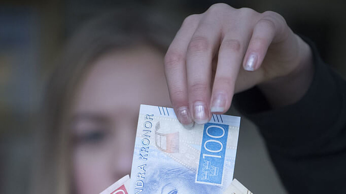 Ung tjej håller i ett gäng svenska sedlar som en solfjäder.