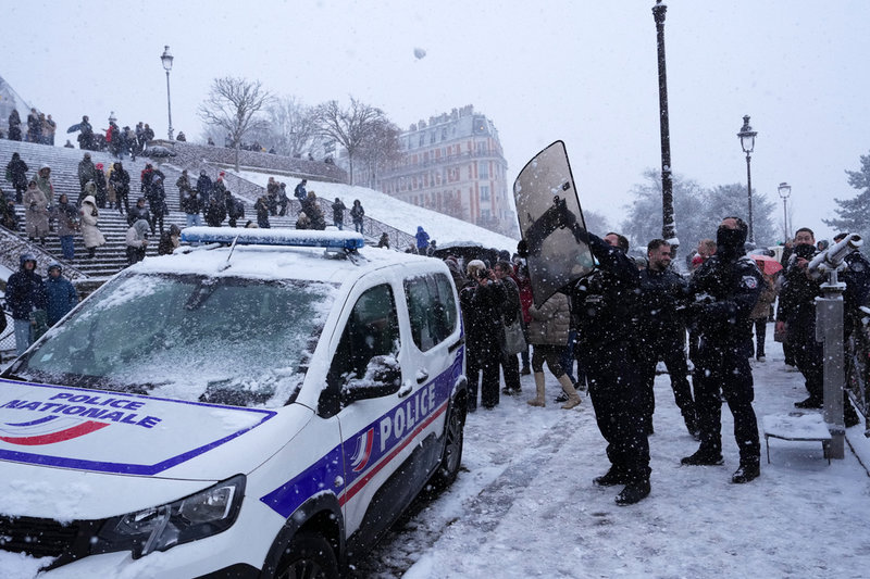 En polis tar skydd från snöbollar vid Sacré-Coeur på måndagen.