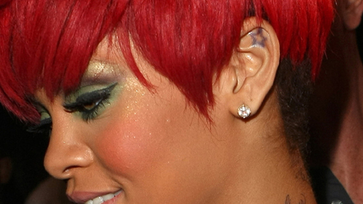 I vänstra toppen av örat, där det ska göra som ondast, har Rihanna en stjärna. Hon har även texten "Rebelle Fleur" på halsen. 