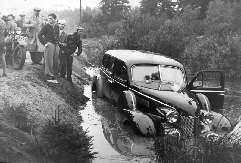 Kung Gustaf V:s Cadillac beskådas av nyfikna åskådare efter att ha hamnat i ett vattenfyllt dike vid Smista strax söder om Segeltorp i Stockholm 1946. Olycksplatsen fick därefter heta Kungens kurva. Arkivbild.