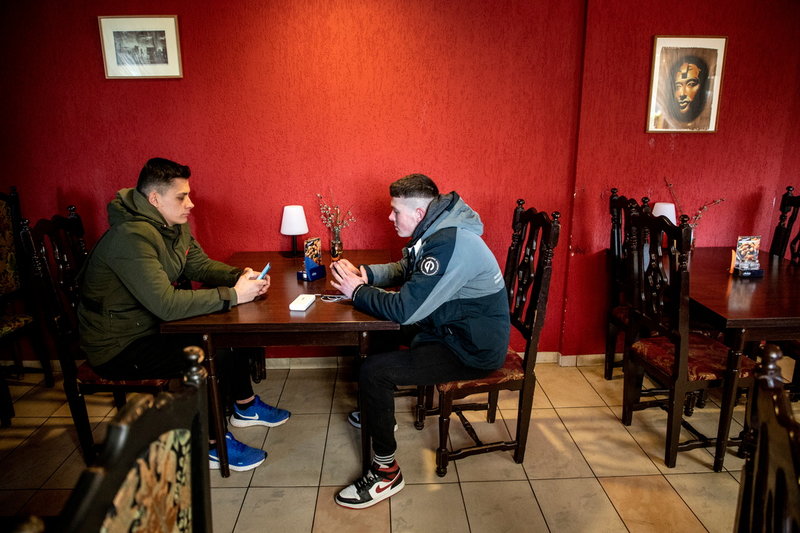 Tonåringarna Denis och Mantas, i grön jacka, scrollar på mobilerna på Panemunes krog.
