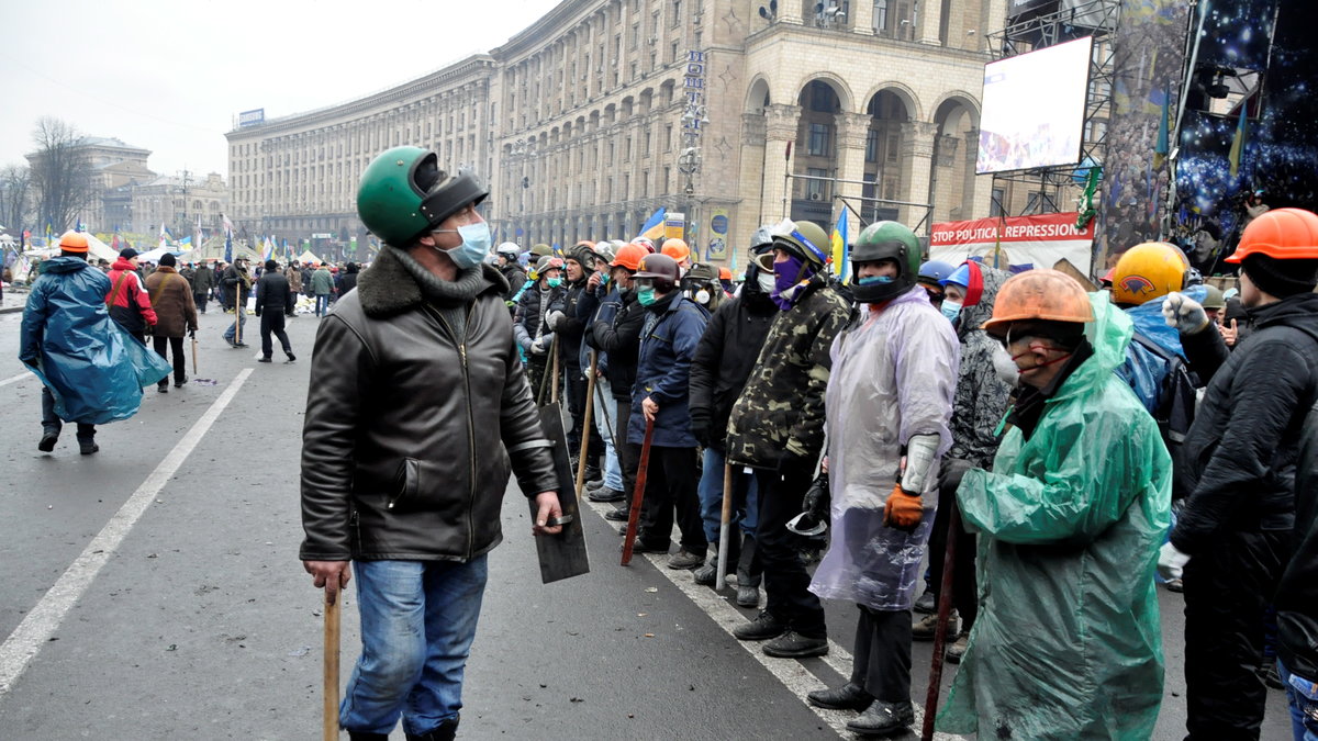 Demonstranter, beväpnade med järnrör och baseballträn, står uppställda framför scenen på Självständighetstorget i Kiev.
