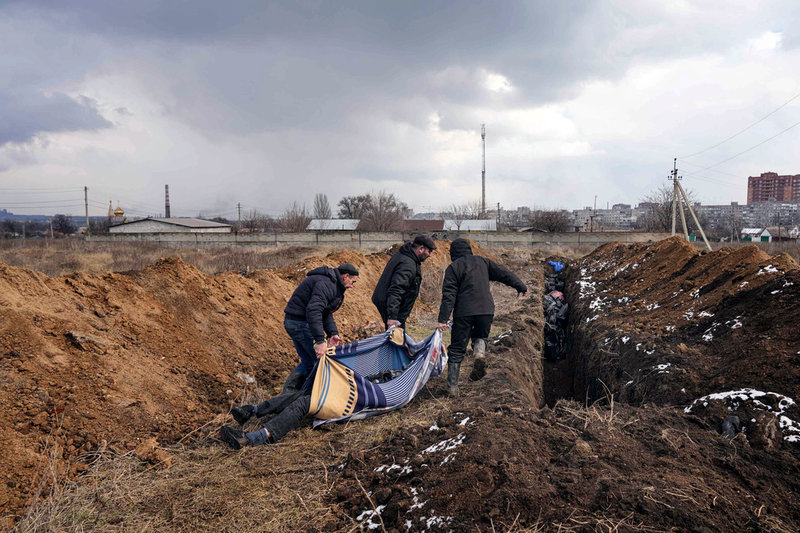 Dödgrävare lägger kroppar i en massgrav i utkanten av Mariupol.