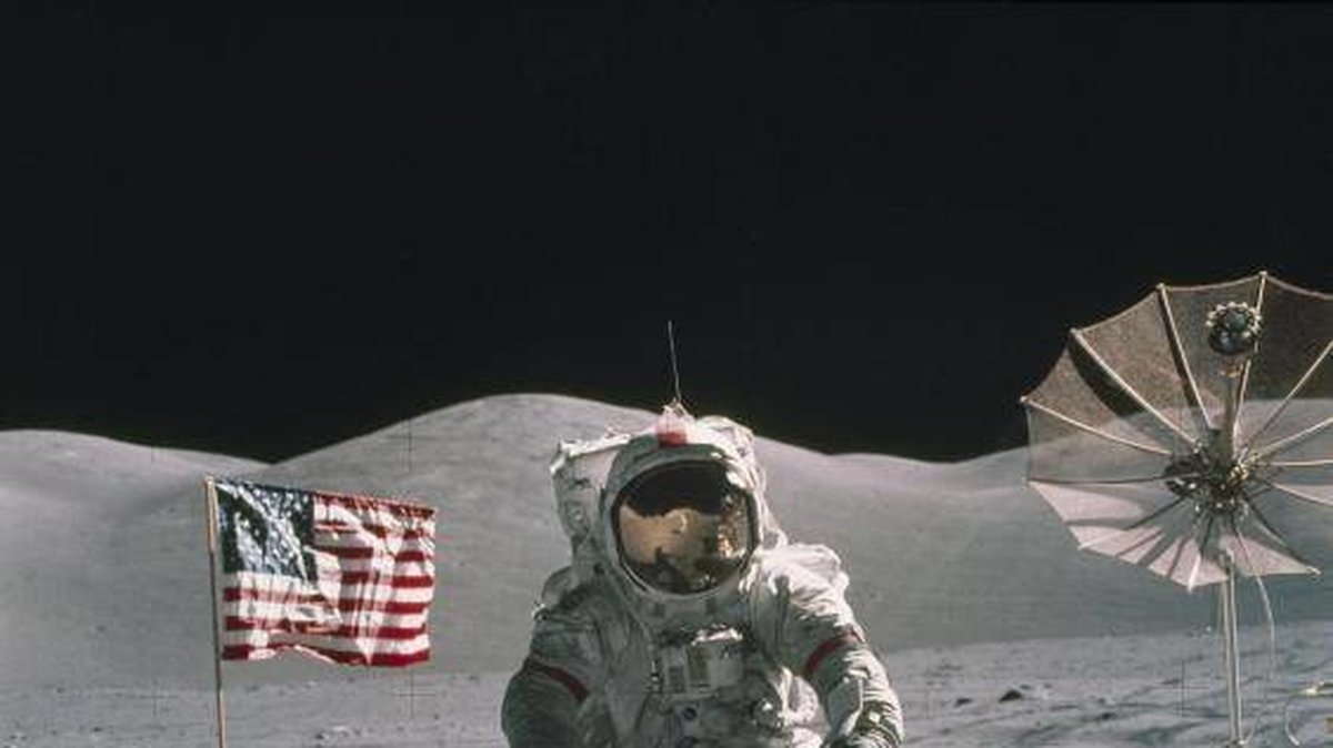 En astronaut står på månen, bredvid den amerikanska flaggan.