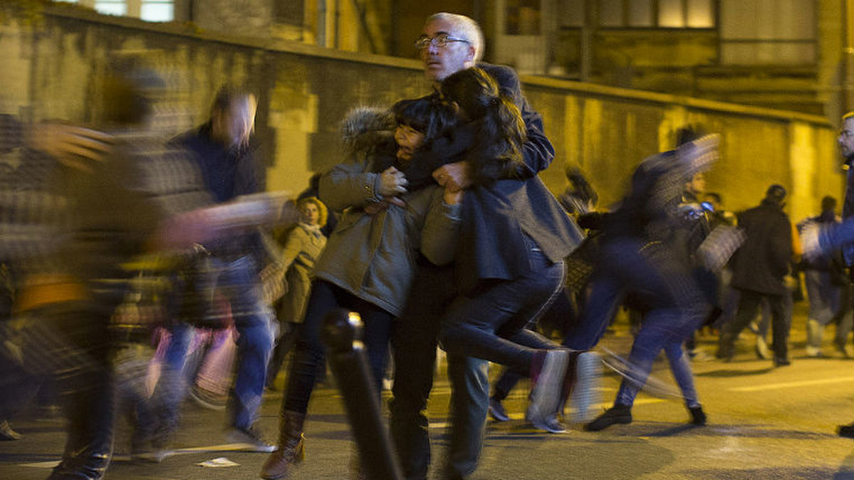 En man försöker skydda sina barn under kaoset i samband med terrordådet i Paris i november 2015.