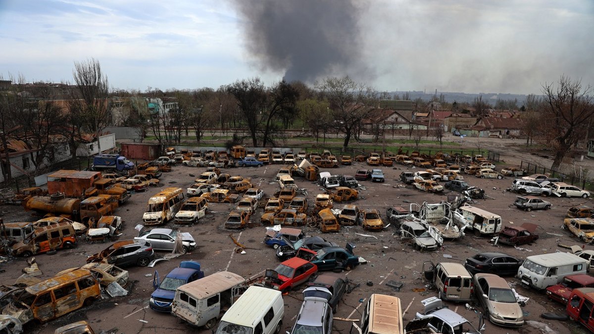 Förstörda och utbrända bilar syns i förgrunden, medan rök stiger från stålverket i Mariupol där kraftiga strider pågått i veckor. Bild tagen 18 april.