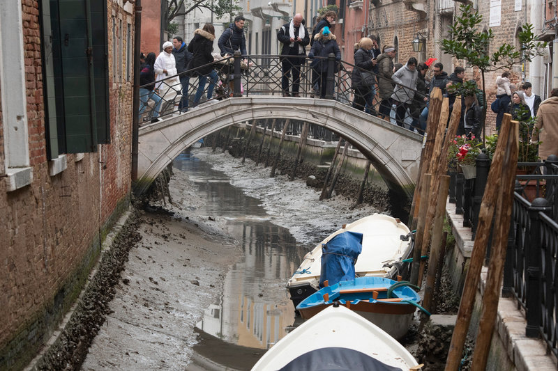 Turister på en av Venedigs många broar inspekterar de torra kanalerna den 21 februari.
