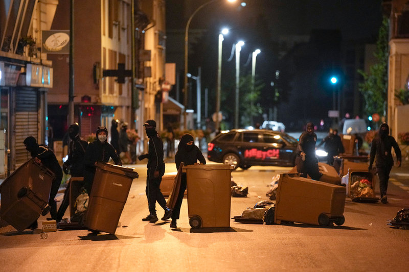 Maskerade personer spärrar av en gata i Colombes utanför Paris med soptunnor natten mot lördagen.