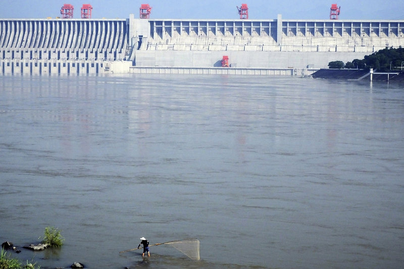 En fiskare med sitt nät syns längst ner i bild, framför dammanläggningen Tre raviner i östra Kina. Dammen ger el, men ska enligt diktaturens myndigheter även kunna hindra översvämningar.