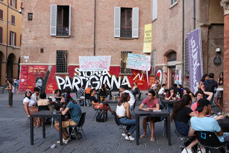 På Piazza Verdi samlas studenter för gatufester, konserter och billig öl. 'Storia partigiana' står det på stenväggen – partisanerna ledde det italienska motståndet under andra världskriget och fångade till slut även in diktatorn Benito Mussolini.